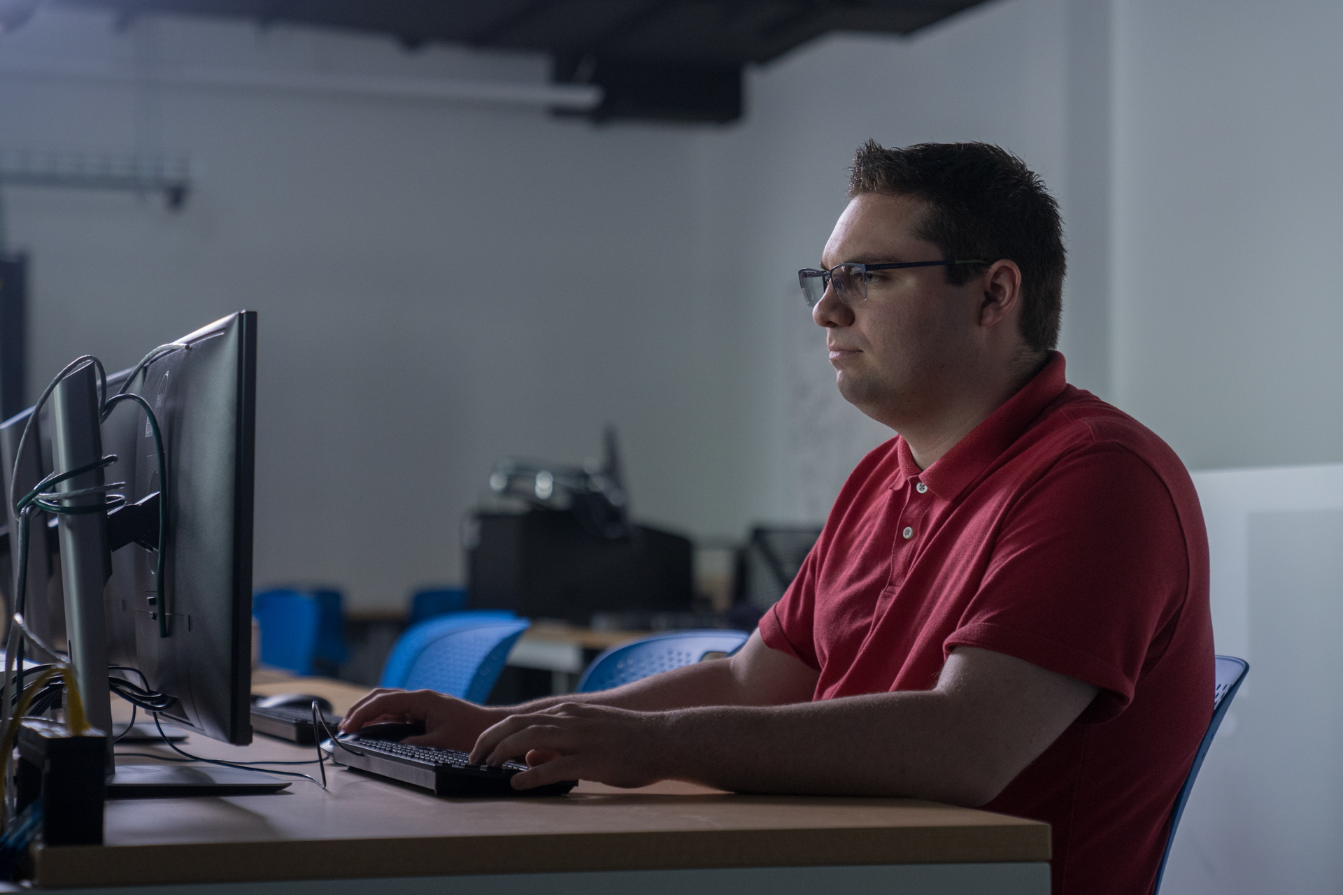 A student in a red shirt is sitting at a computer.