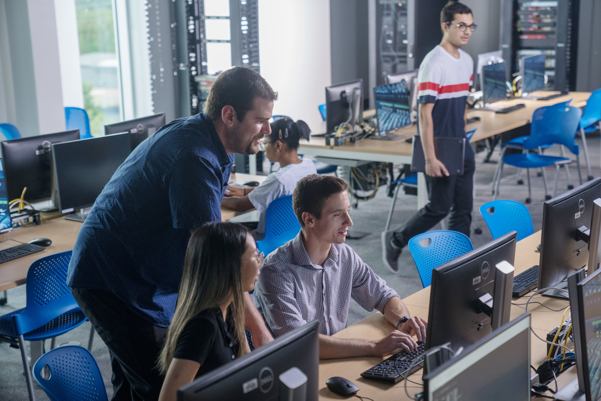 Two students and one professor are looking at a computer.