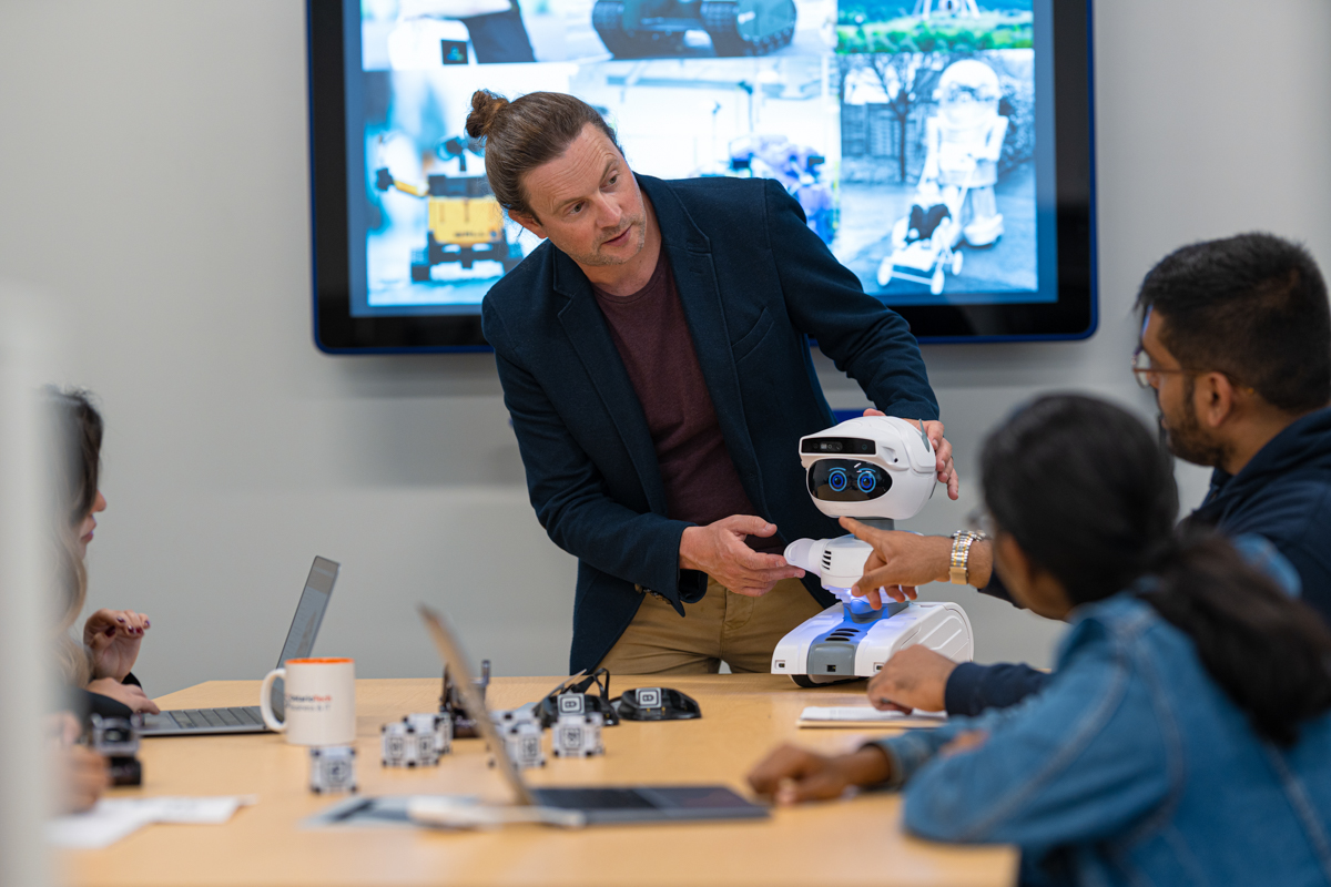 A professor is displaying a small robot on a table to students.