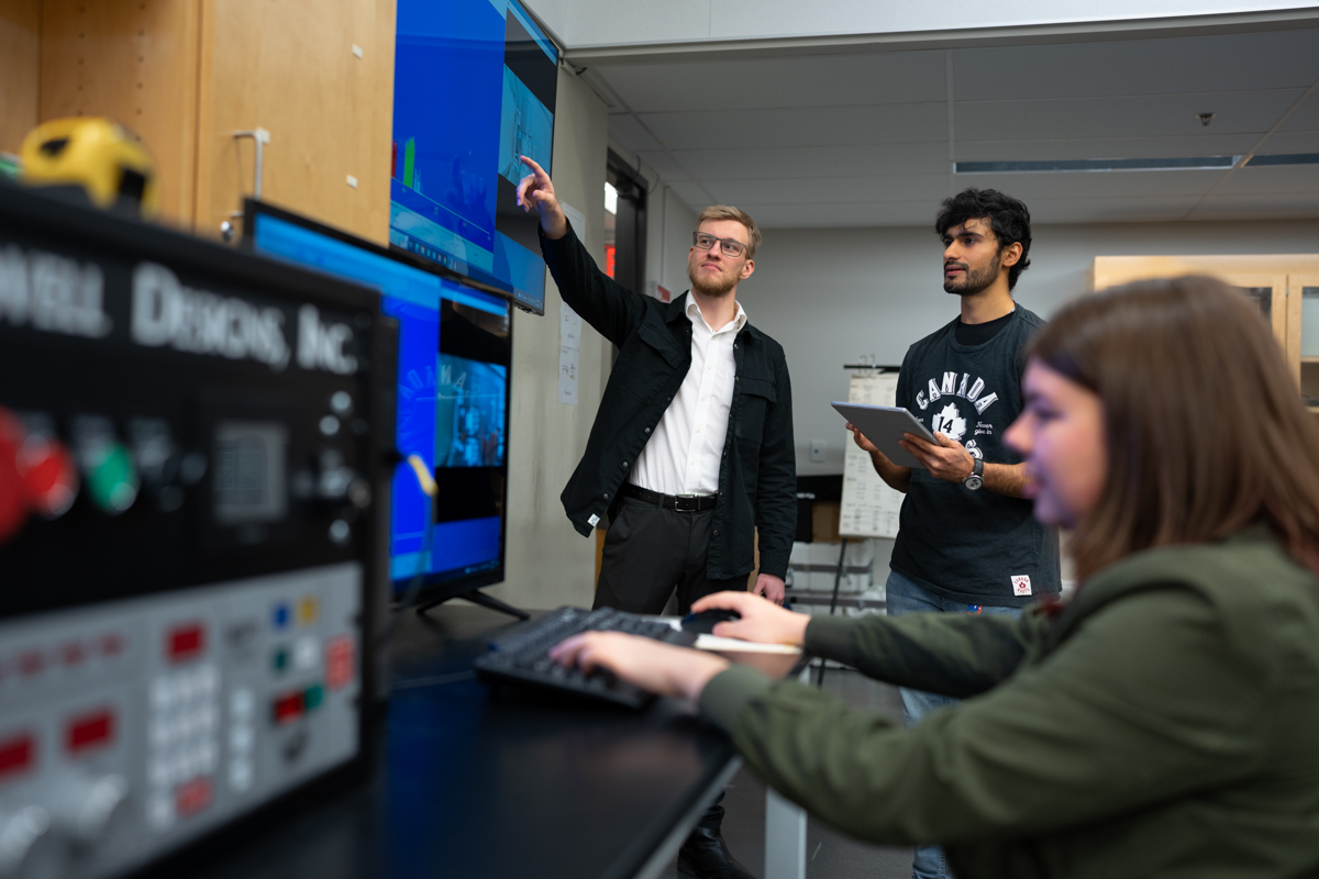 A professor is guiding students through the use of engineering technology.