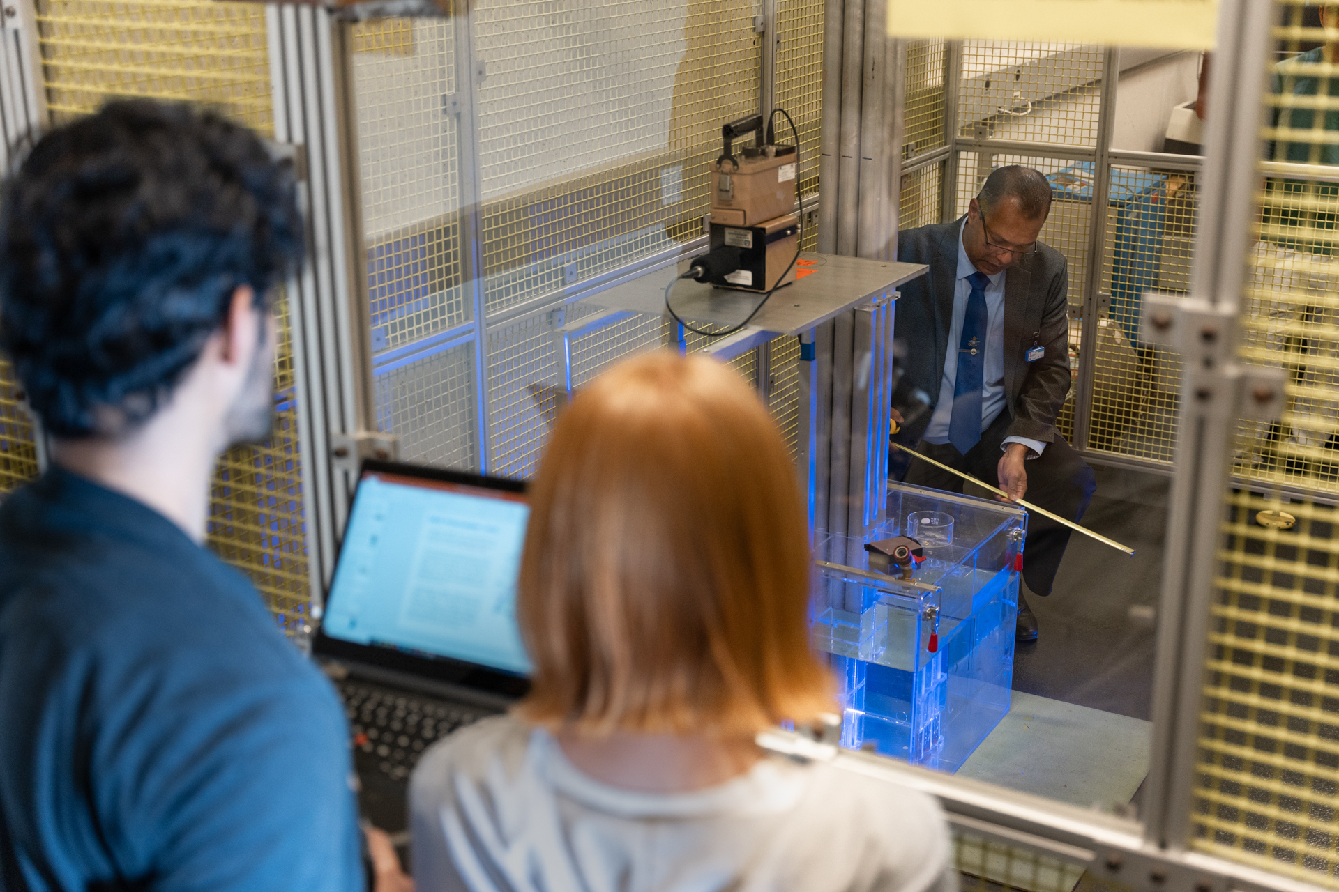 Two students are watching a professor work on engineering technology.
