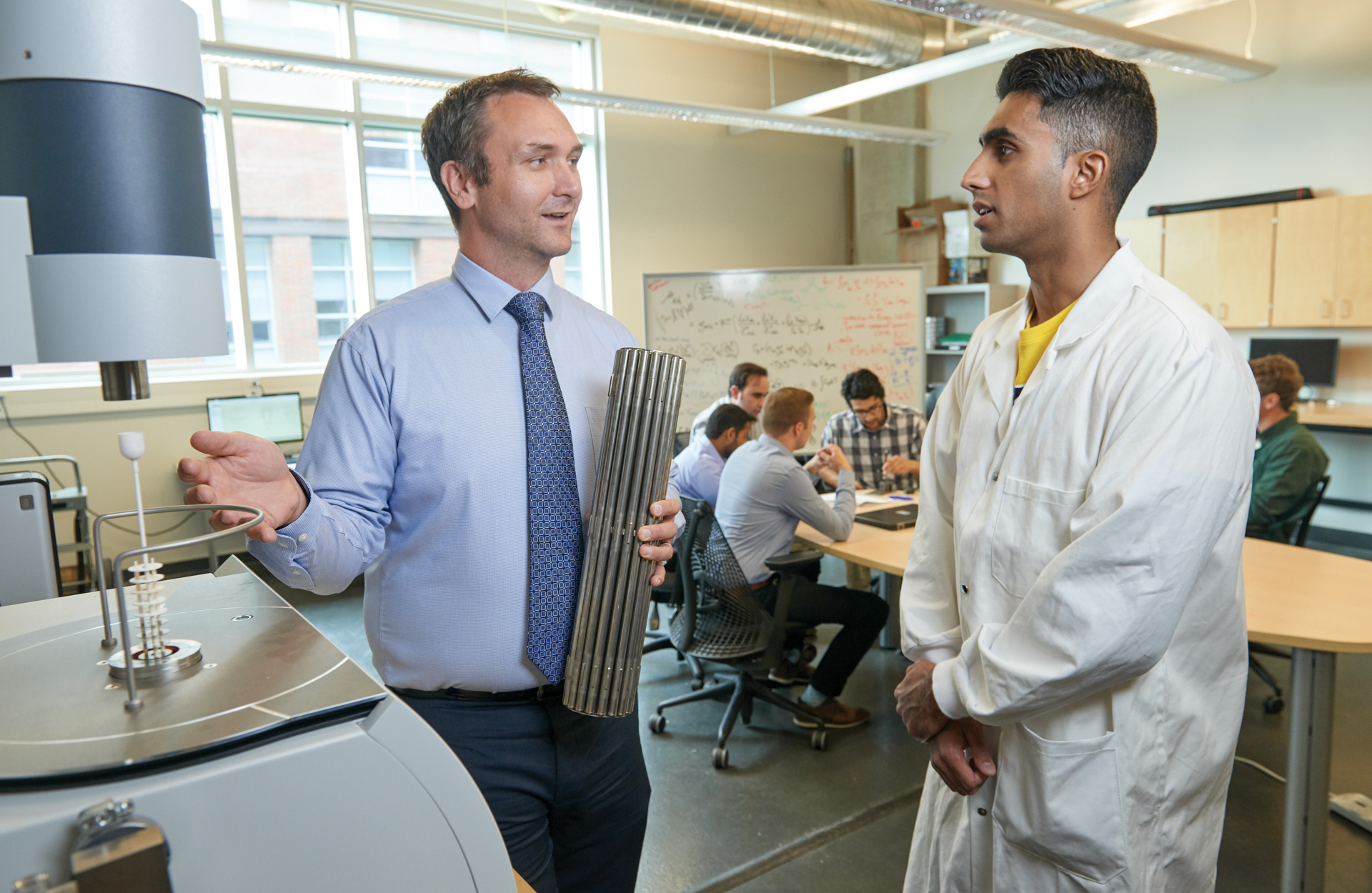 A professor guides a student alongside engineering equipment.