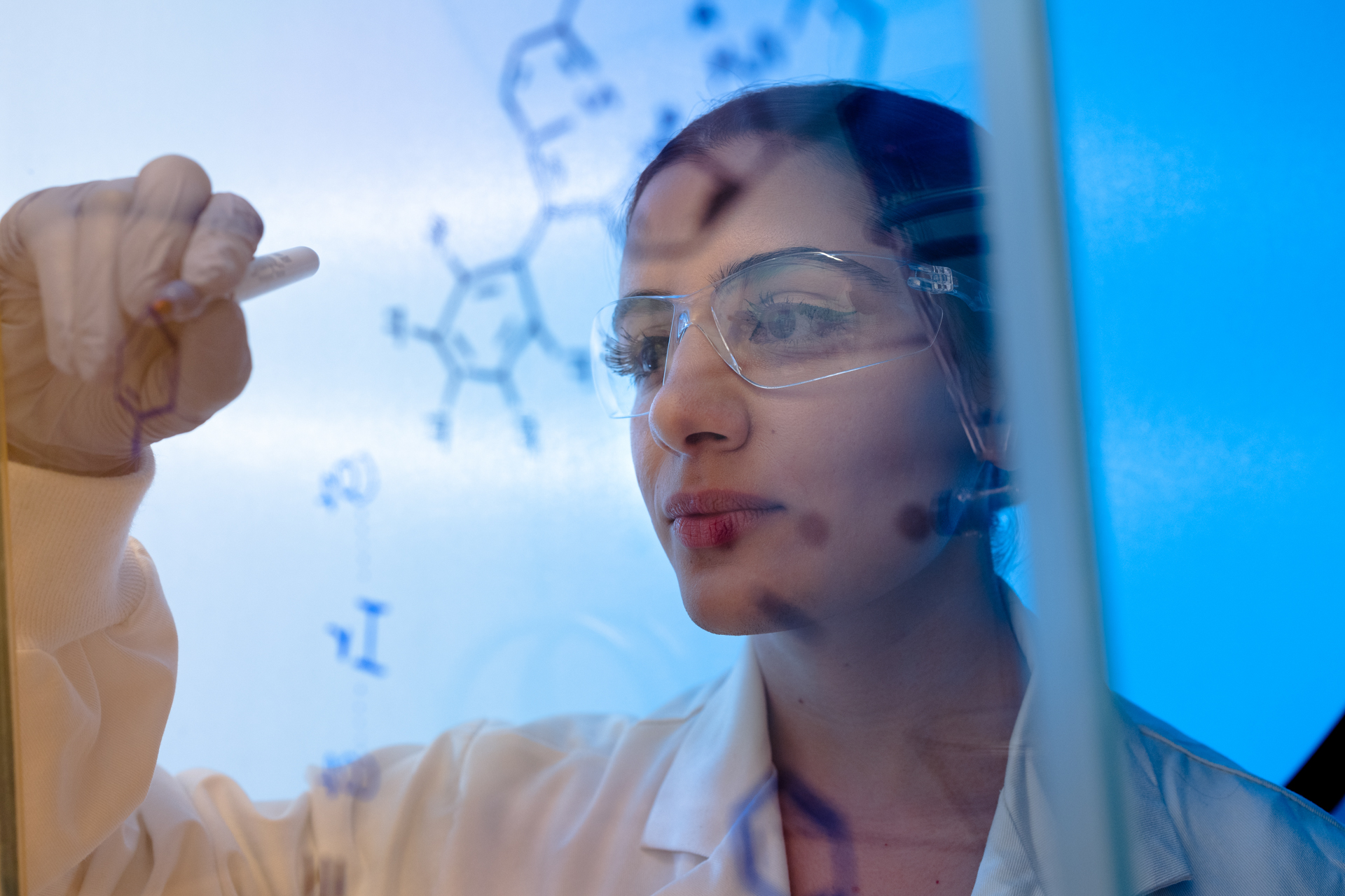 A female scientist writes out scientific symbols on a board.