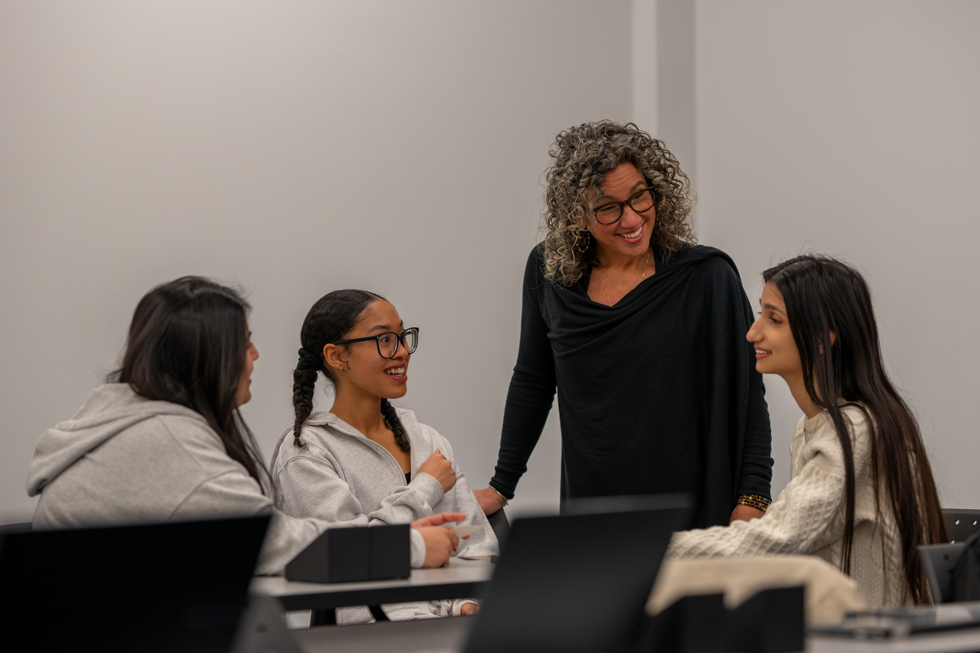 A professor stands at a table speaking with students