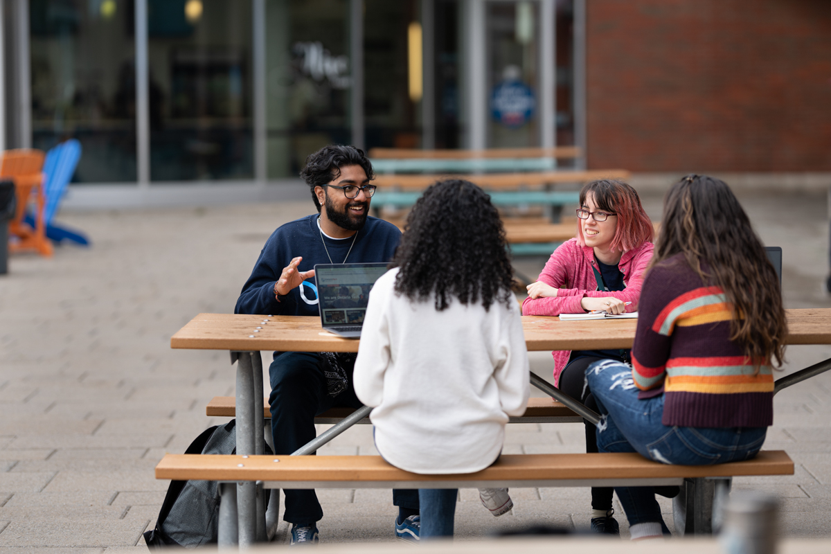 Students sitting outside at a picnic table sharing in a meal and conversation together