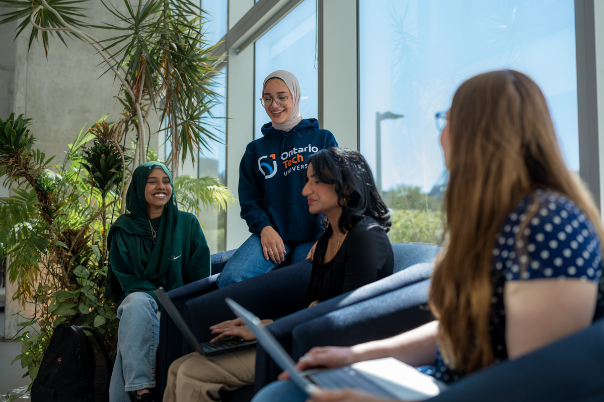 Students sitting inside talking and looking at computer.