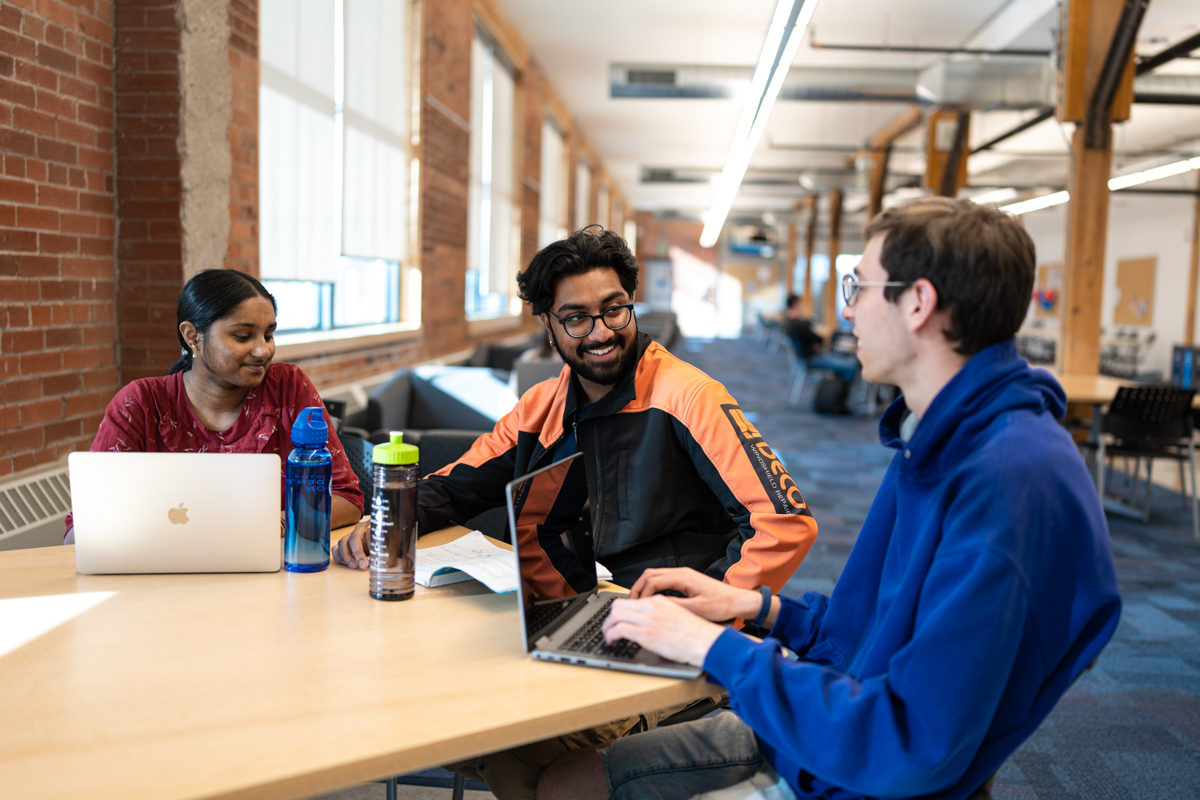 a person seated at a computer smiling and sitting with two colleagues