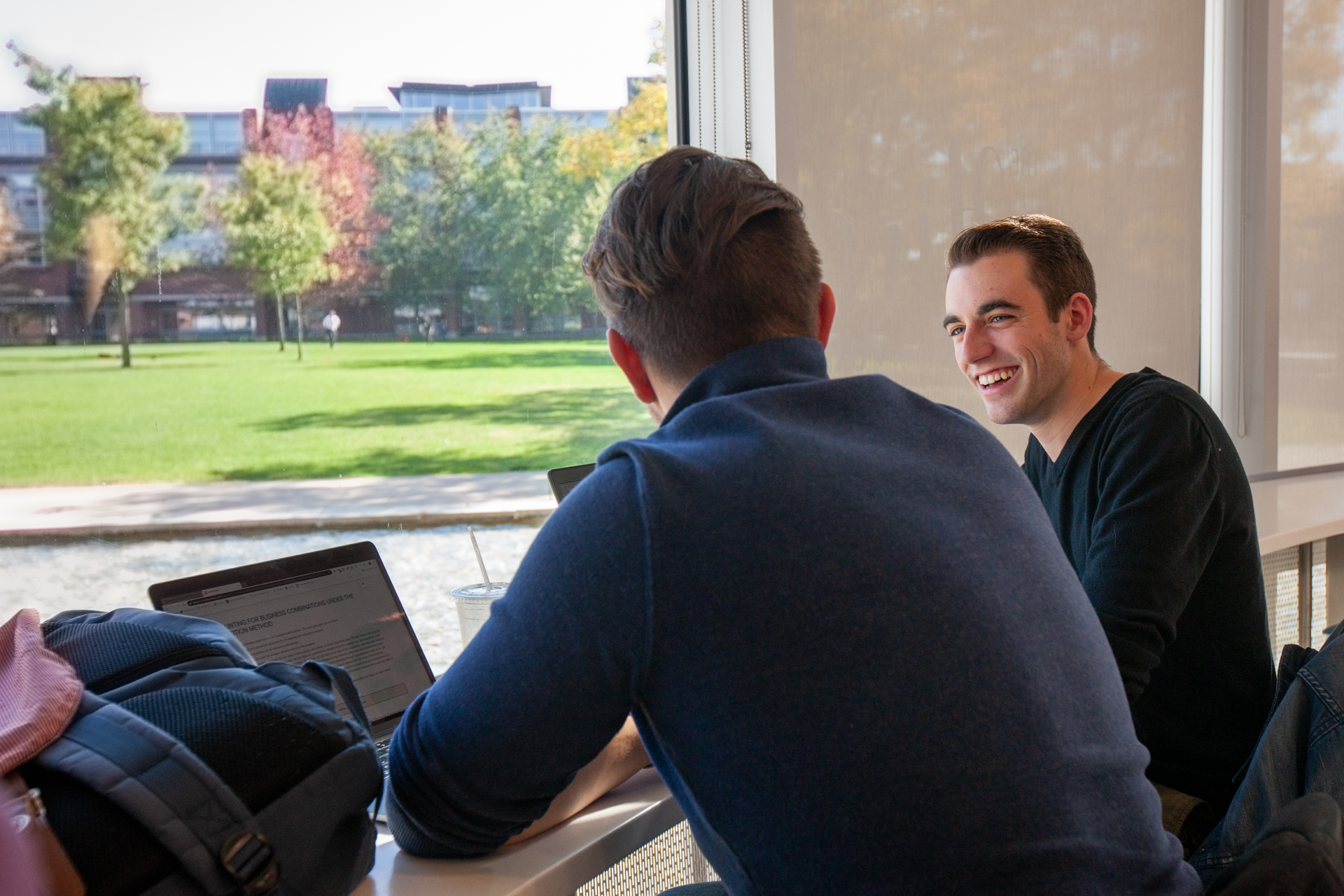 Two students are seated at a table talking and smiling
