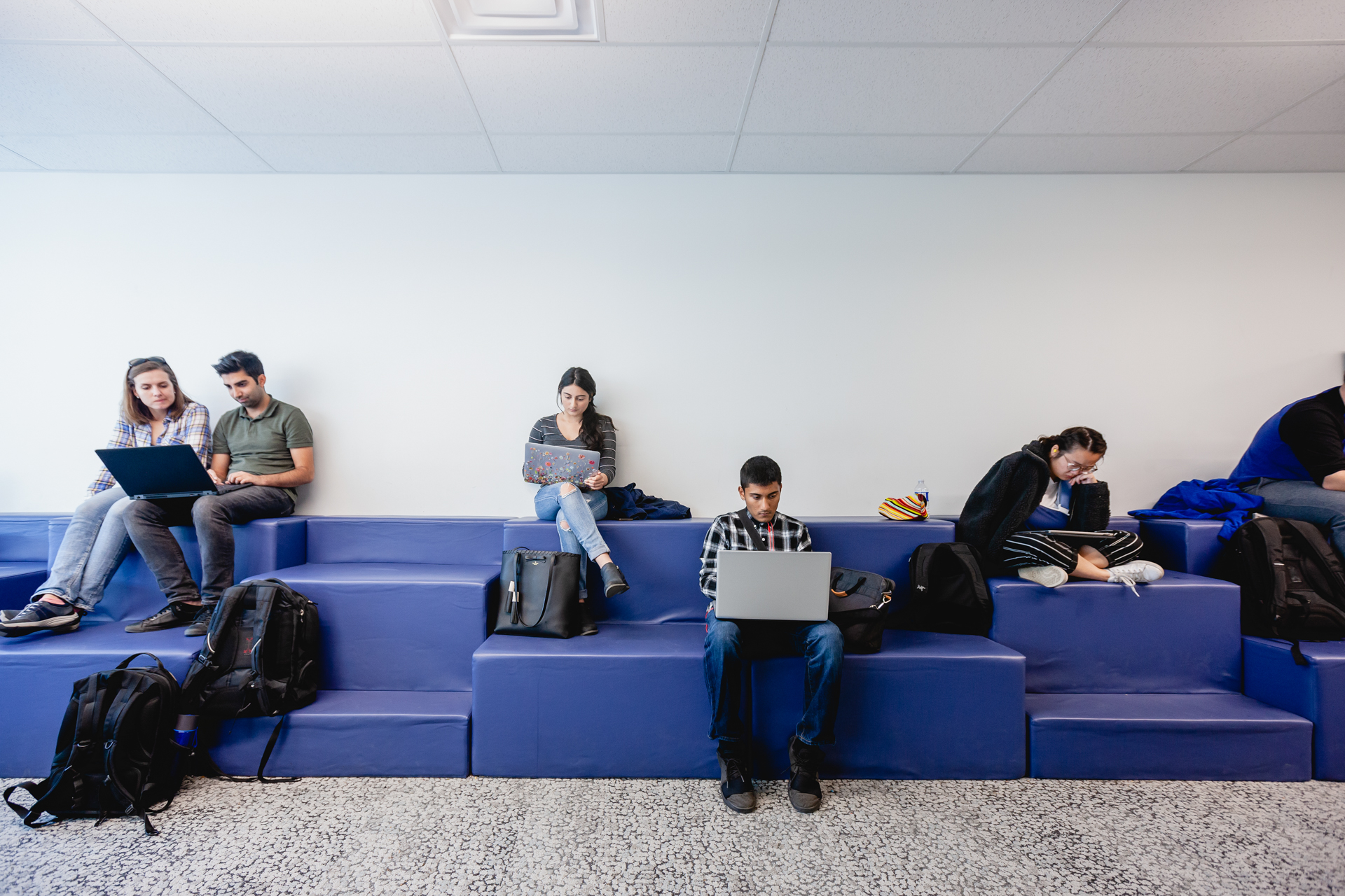 A group of students are sitting on a bench and studying separately on laptops.
