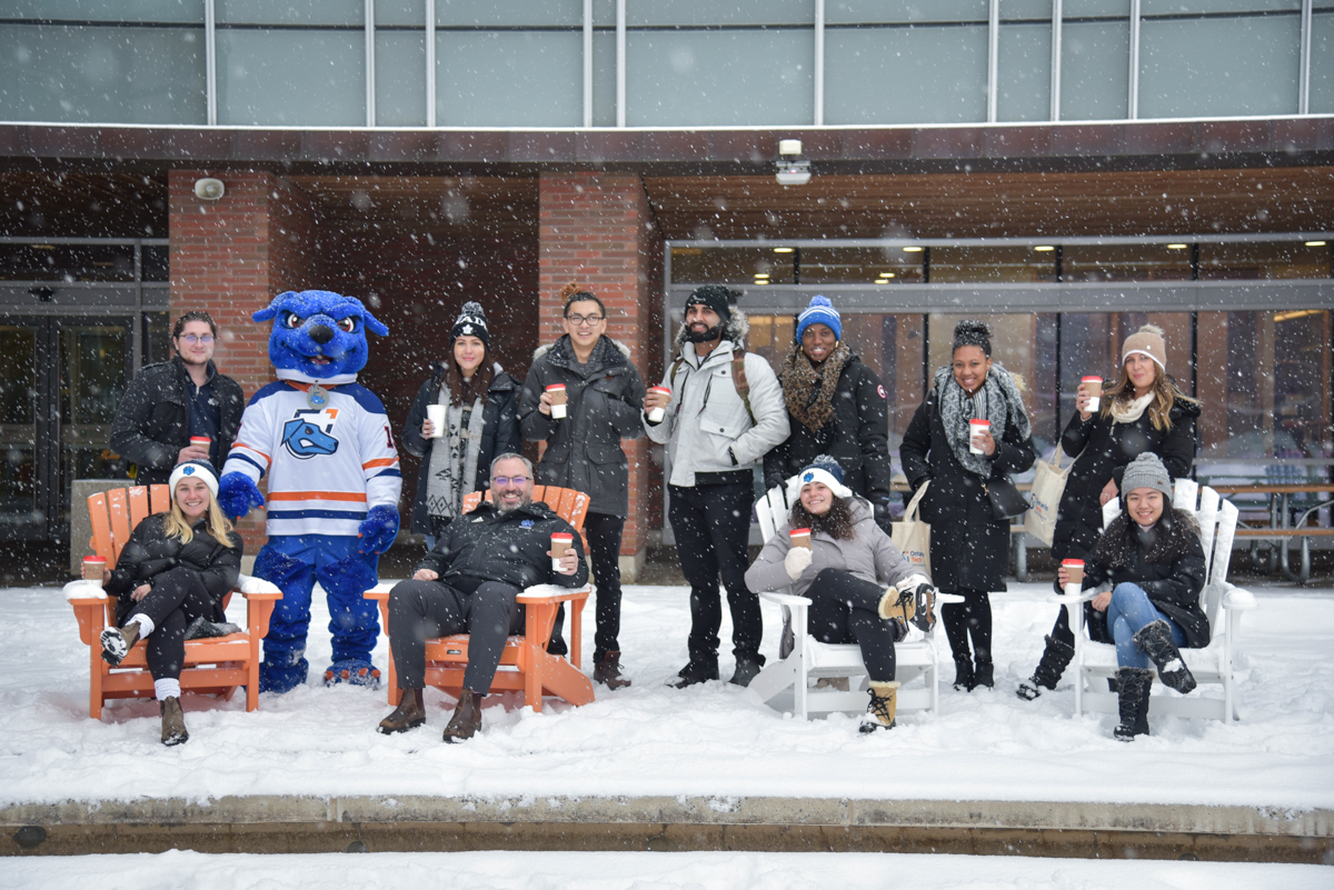 Ontario Tech employees and staff sitting outside the library, in the snow, with mugs.