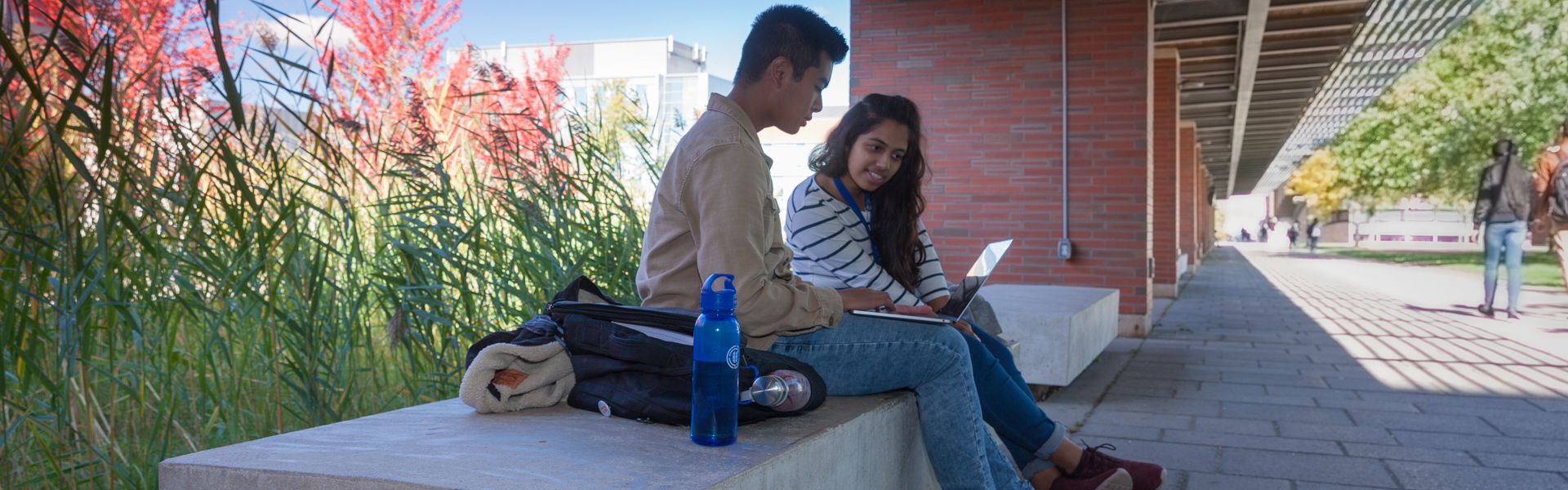 Two students looking at a laptop screen outside
