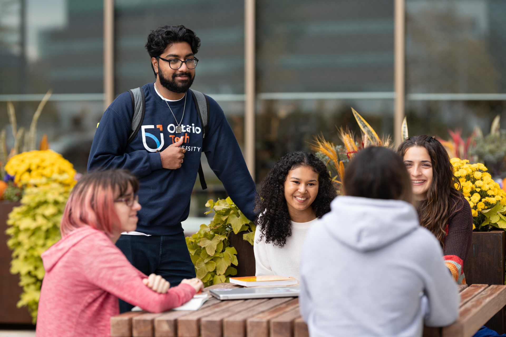 Students smiling in a circle together while sitting at a table outdoors